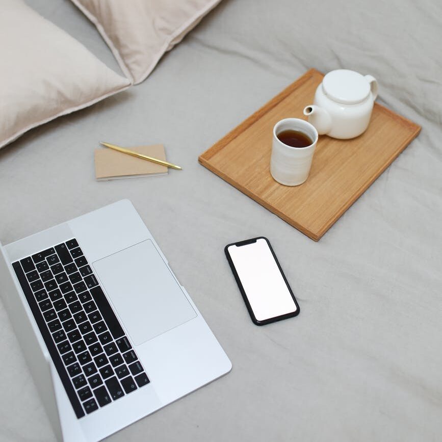 netbook and smartphone placed on bed near tray with tea set while studying for college